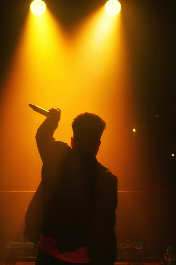 Dynamic silhouette of a male singer performing under warm stage lights.